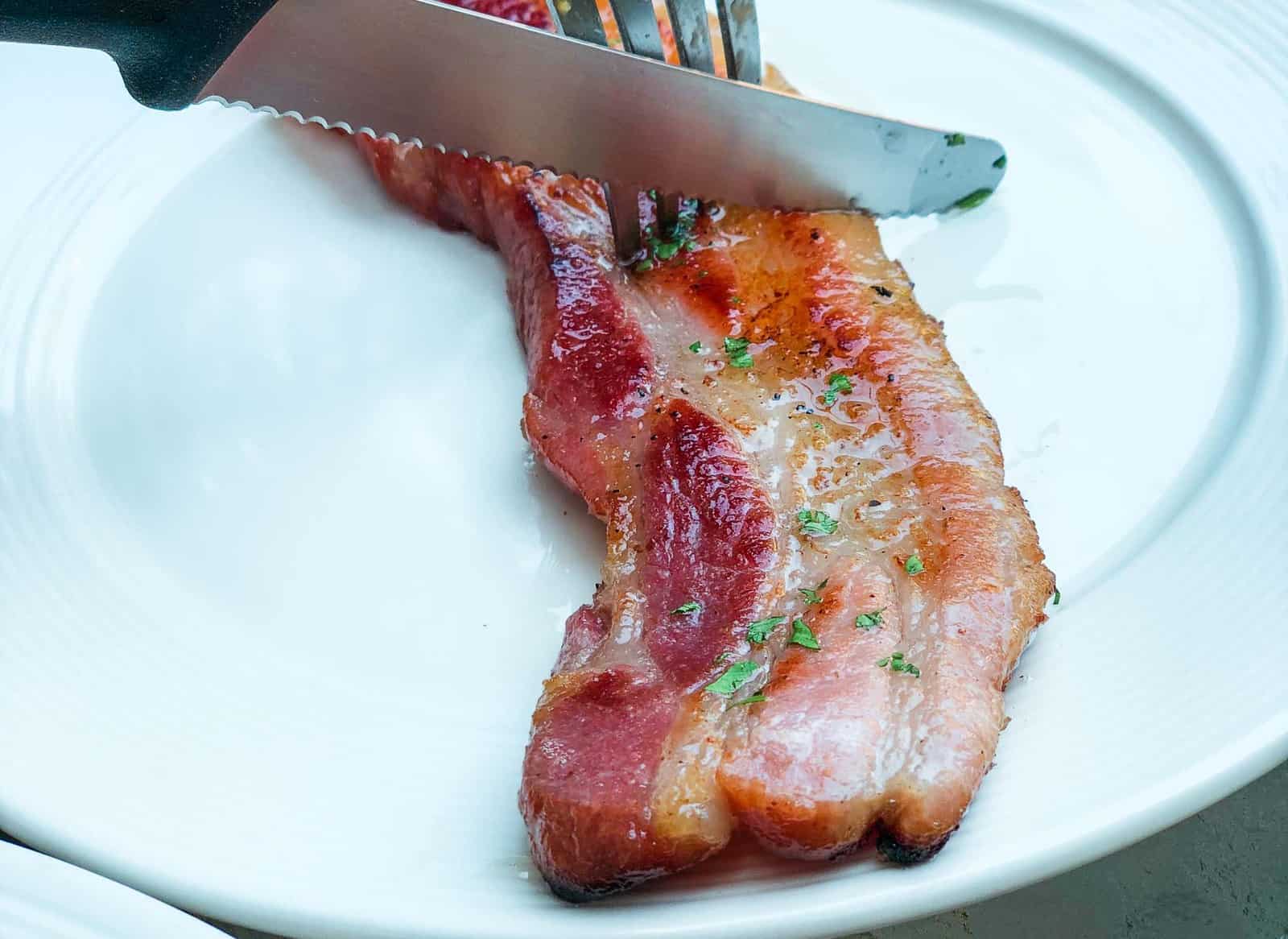 Cutting a piece of thick cut bacon during brunch at Larder Cafe in Chiang Mai, one of the best breakfast spots in Chiang Mai.