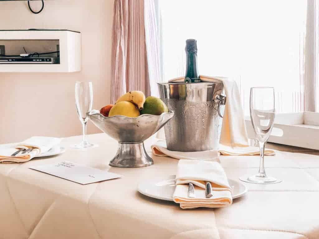 Bowl of fruit and champagne in a bucket on a table in a hotel room. 