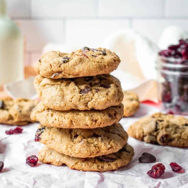 A stack of chocolate cranberry oatmeal cookies on a piece of parchment paper with cranberries and chocolate chips scattered around it.