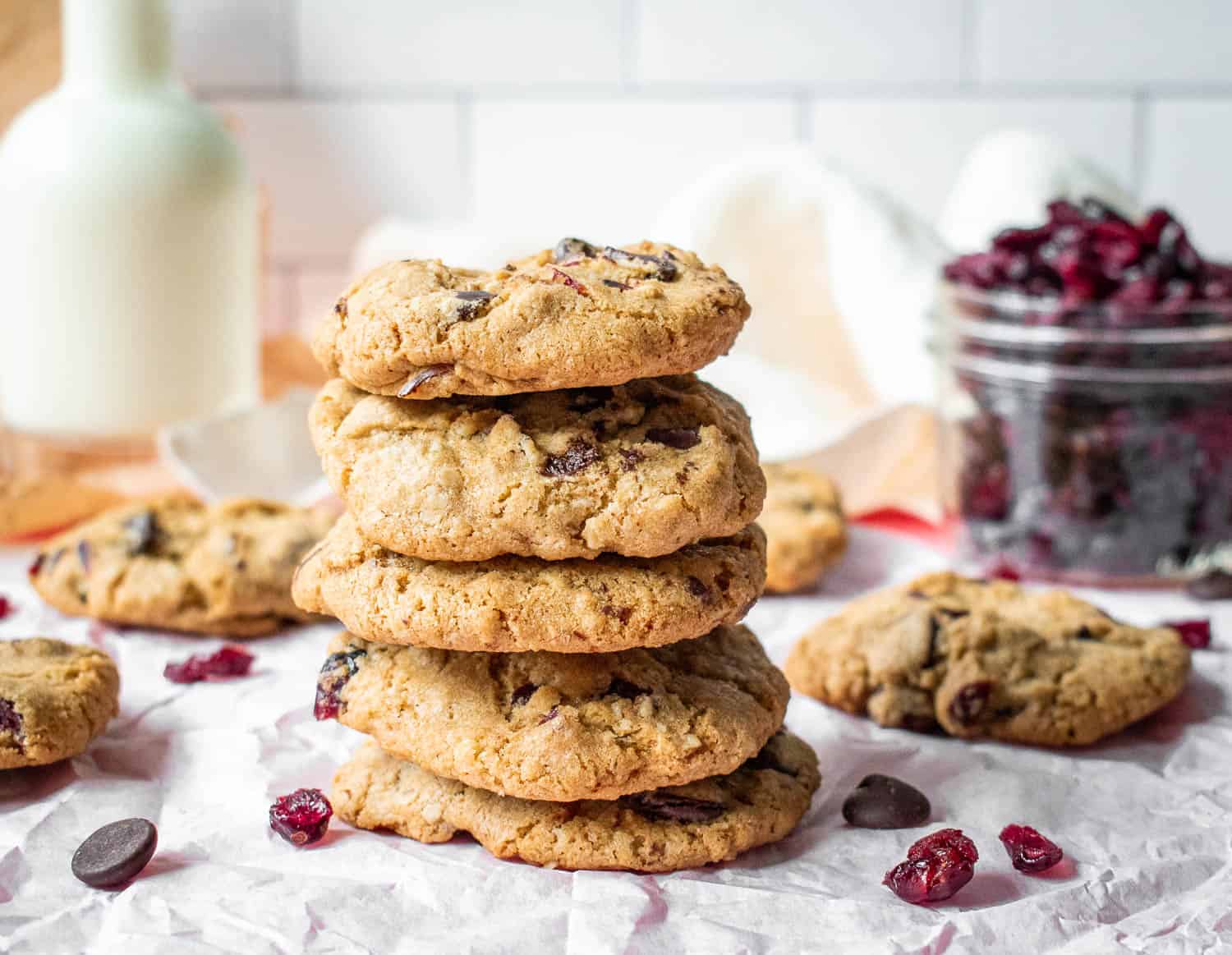 A stack of chocolate cranberry oatmeal cookies on a piece of parchment paper with cranberries and chocolate chips scattered around it.