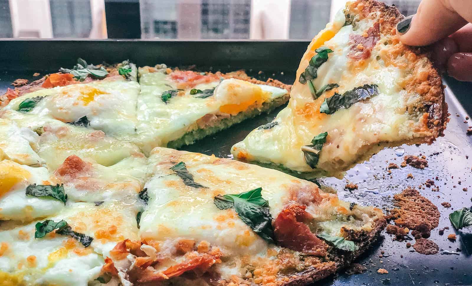 Slice of homemade breakfast pizza being lifted off a tray