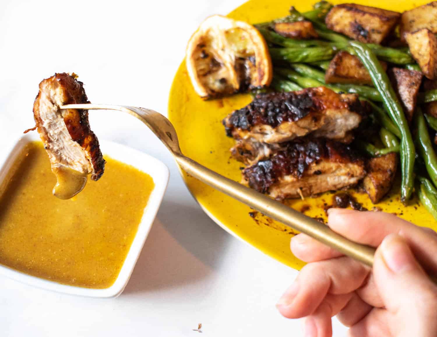 Gluten-free airy fryer honey mustard chicken thighs on a fork being dipped into a side of sauce