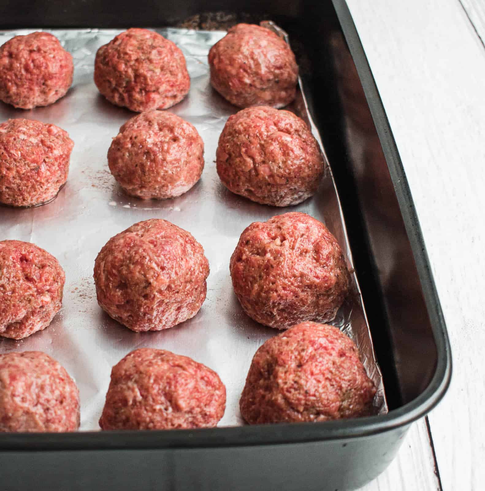 Raw meatballs on a baking sheet about to go into the oven