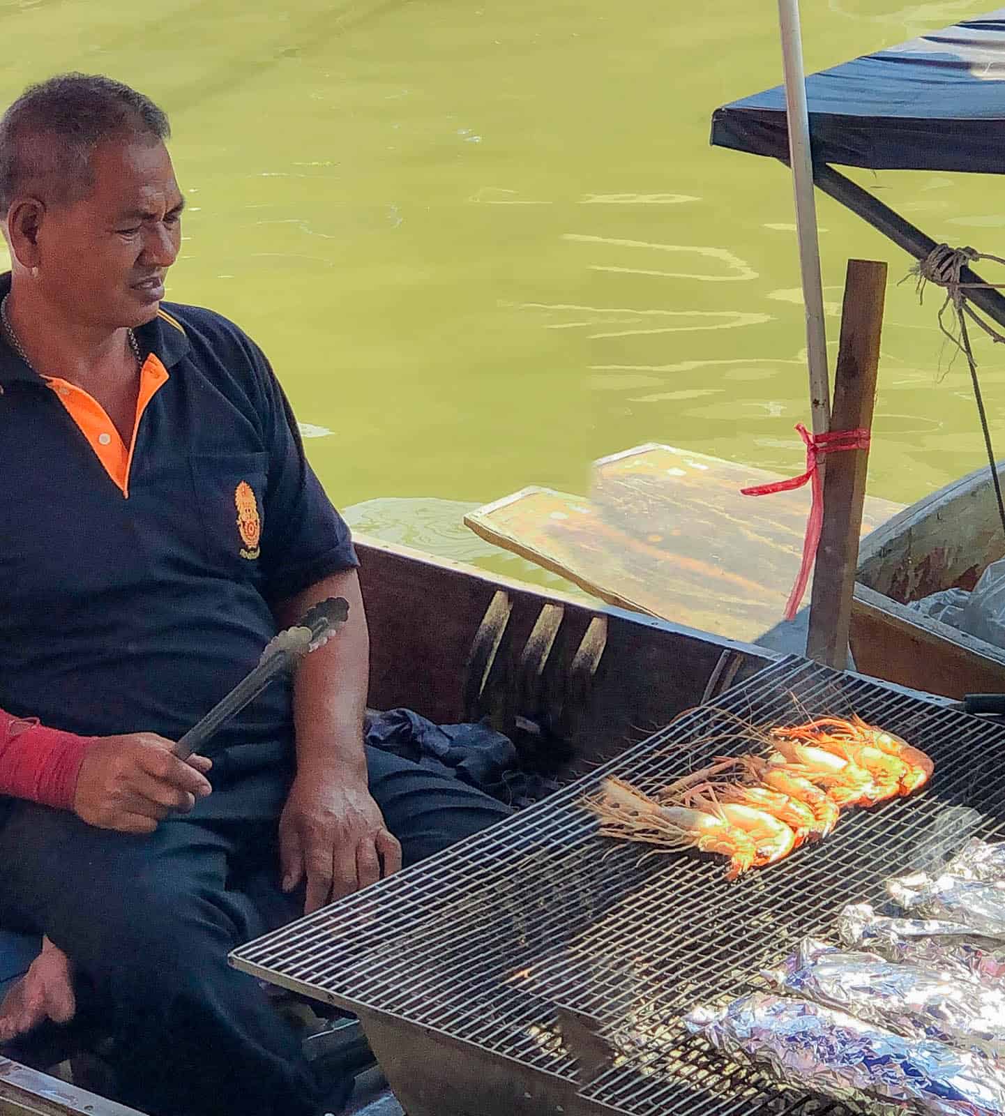 Man grilling fish on a boat at Amphawa Floating Market in Bangkok