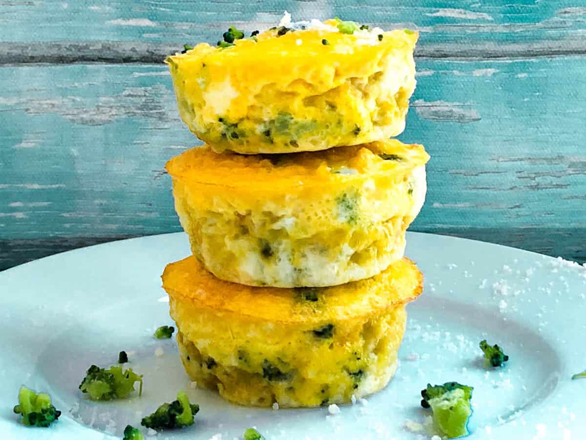 Stack of egg muffins on a plate garnished with broccoli and parmesan cheese. 