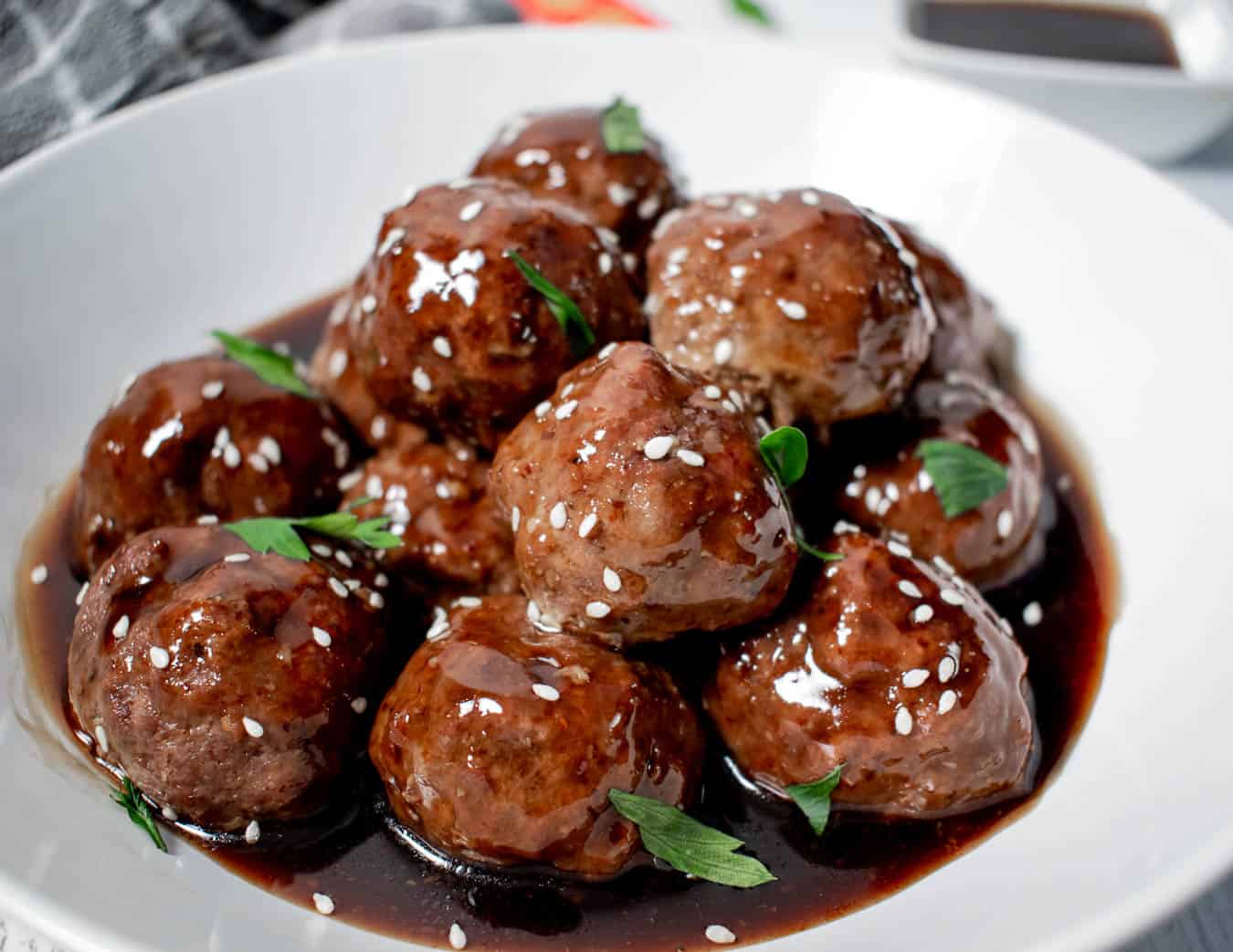 Sticky Asian meatballs recipe - bowl of meatballs in sticky sauce with sesame seeds and garnish. 