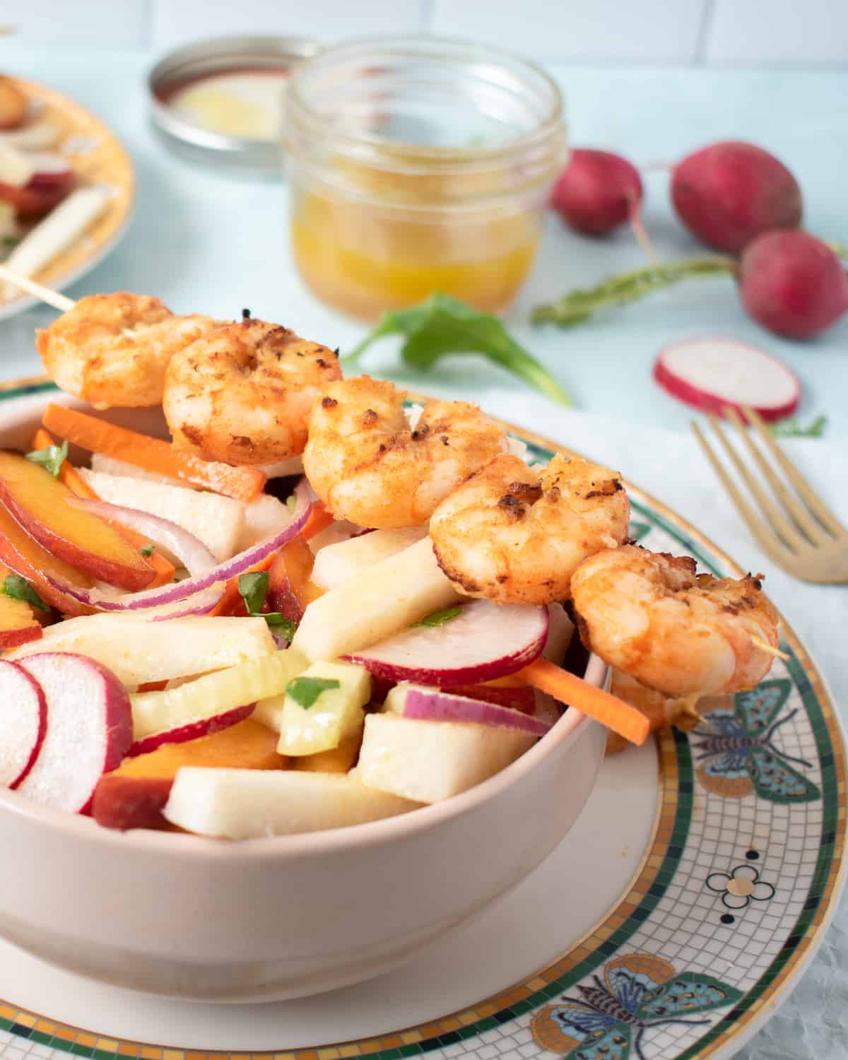 A bowl of crunchy jicama peach salad with shrimp skewers resting on the bowl. 