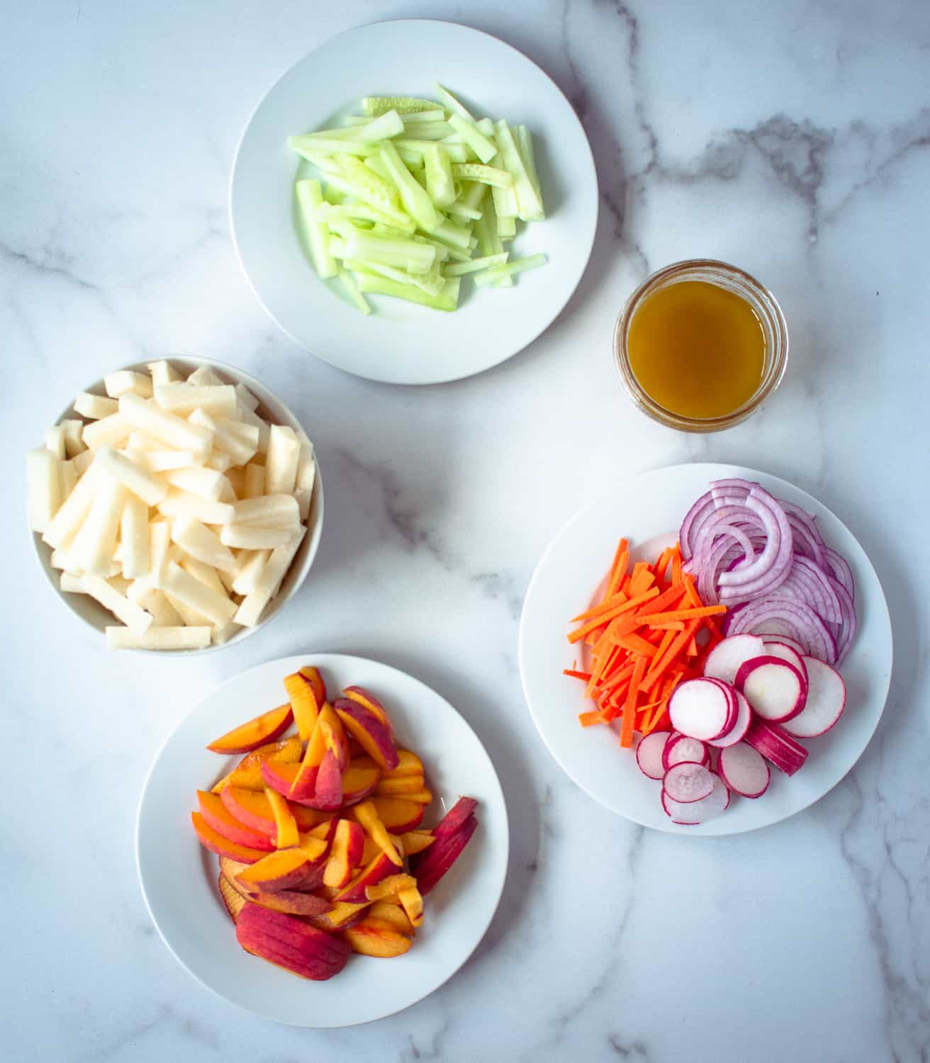 Plates of peaches, carrots, radishes, jicama and cucumber sticks and a jar of honey-lime vinaigrette. These are the ingredients for jicama peach salad. 