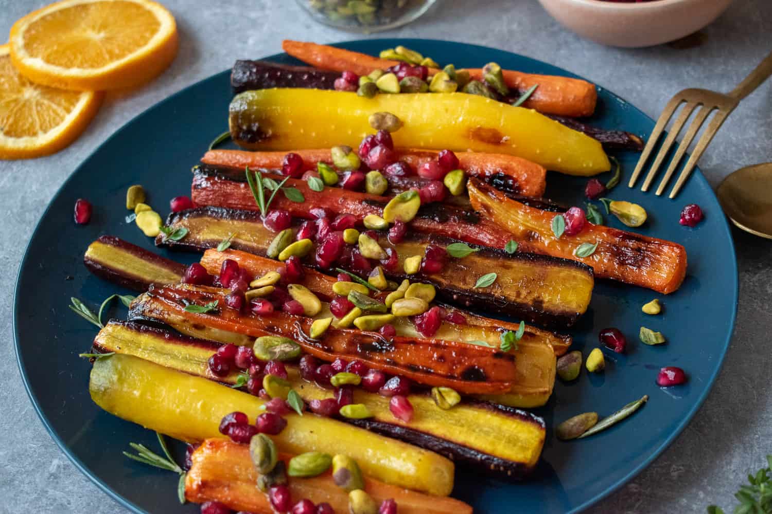 A plate of orange-honey glazed roasted carrots topped with pomegranate seeds and pistachios. 