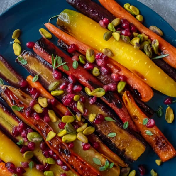 Plate of roasted rainbow heirloom carrots with orange-honey glaze, pomegranate seeds and pistachios.