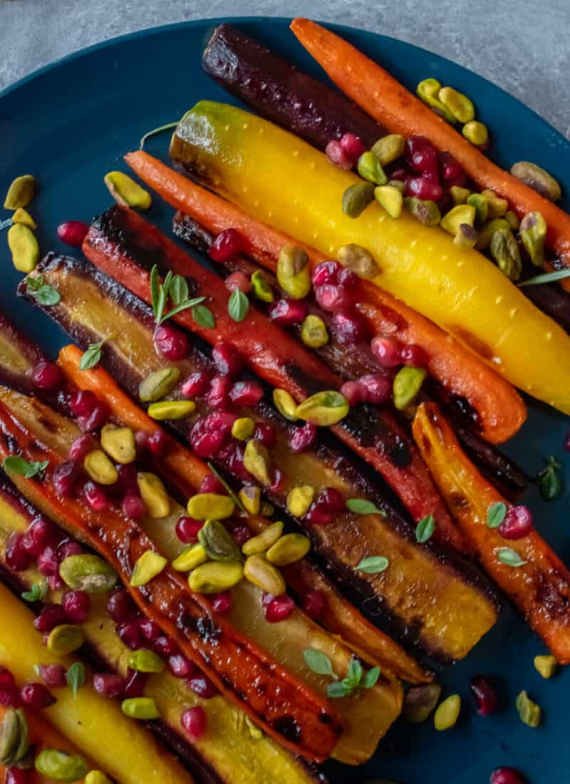 Plate of roasted rainbow heirloom carrots with orange-honey glaze, pomegranate seeds and pistachios.