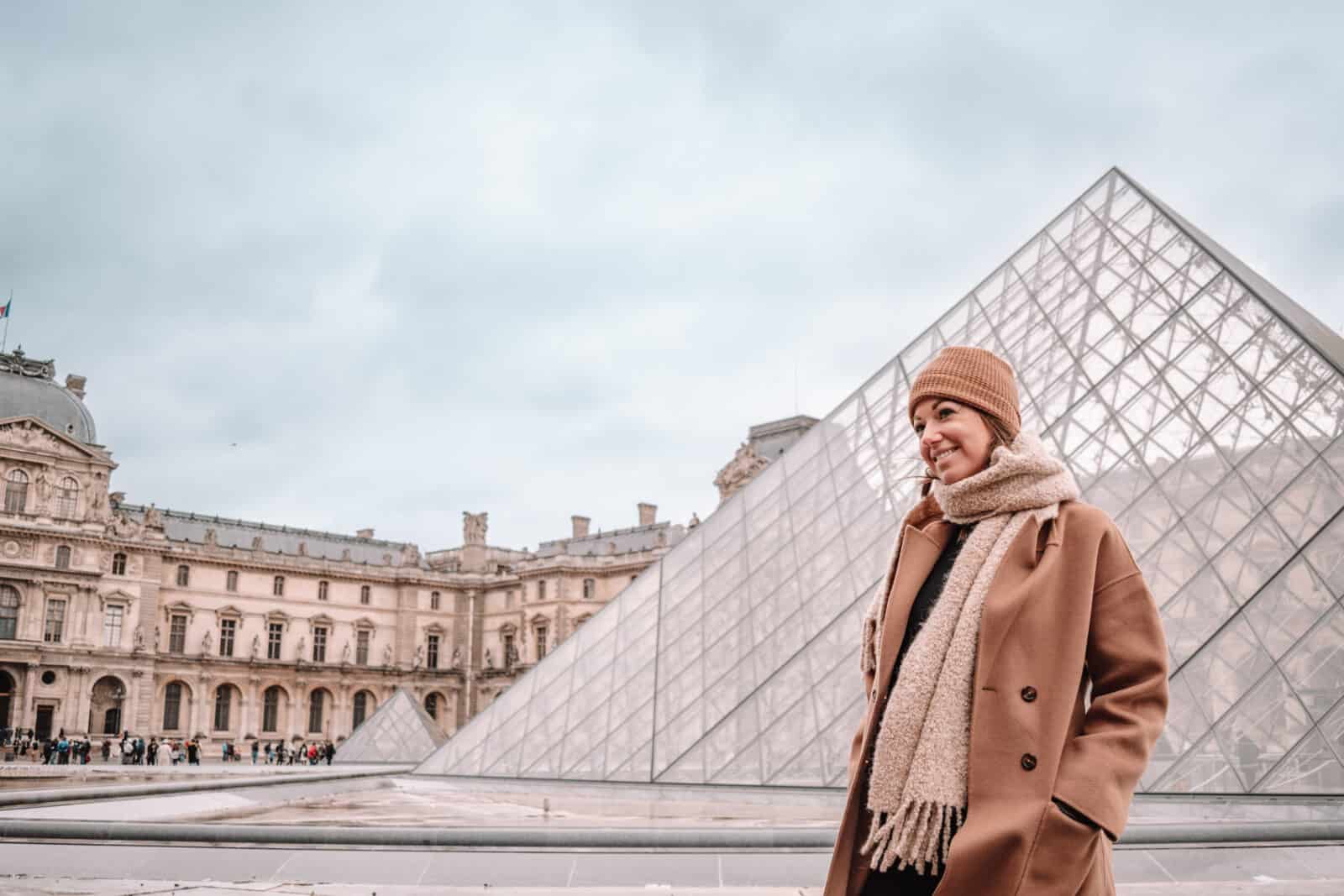 A woman standing outside the Louvre in Paris, dressed in winter clothing. 