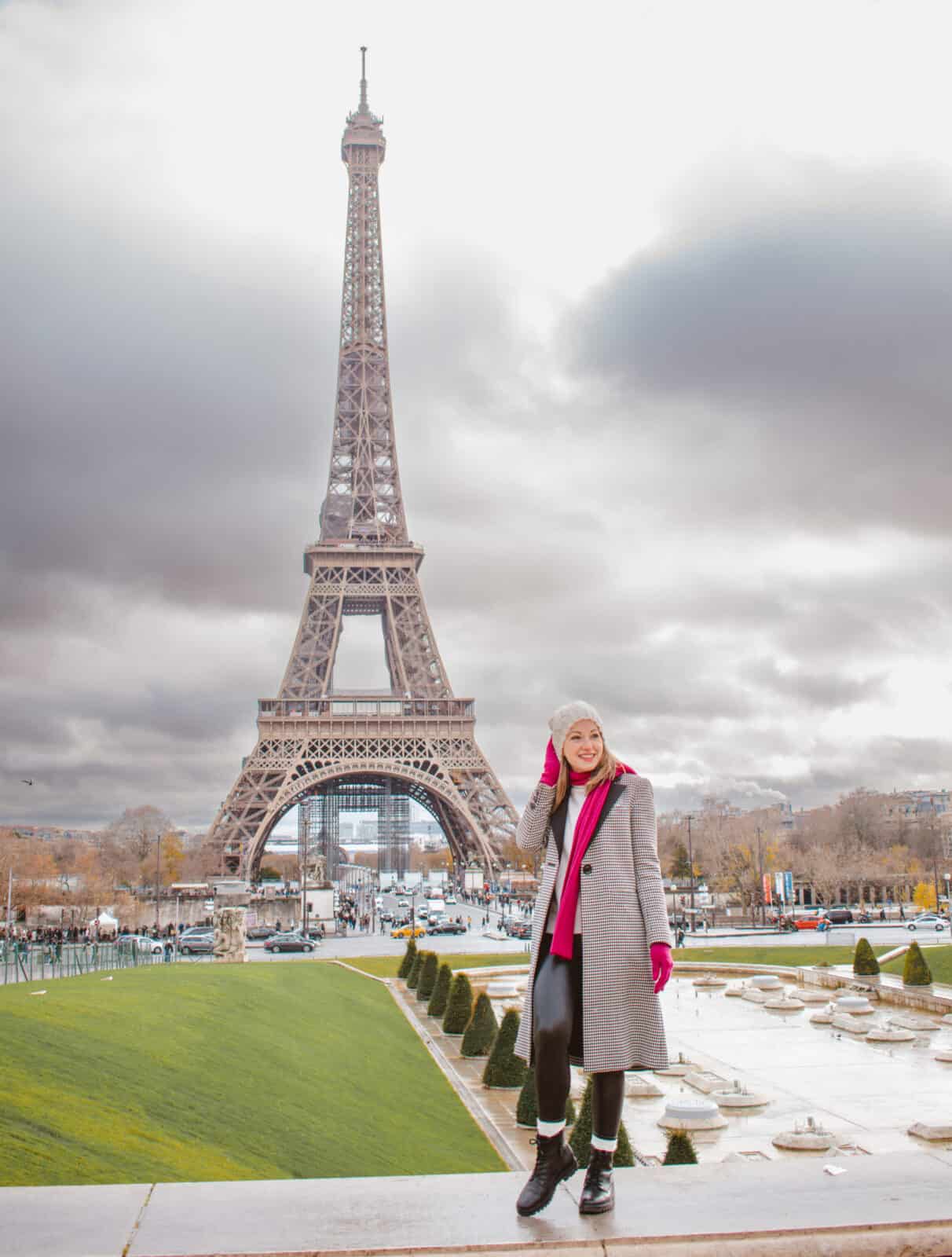 A woman standing in front of the Eiffel tower when visiting Paris in winter. 