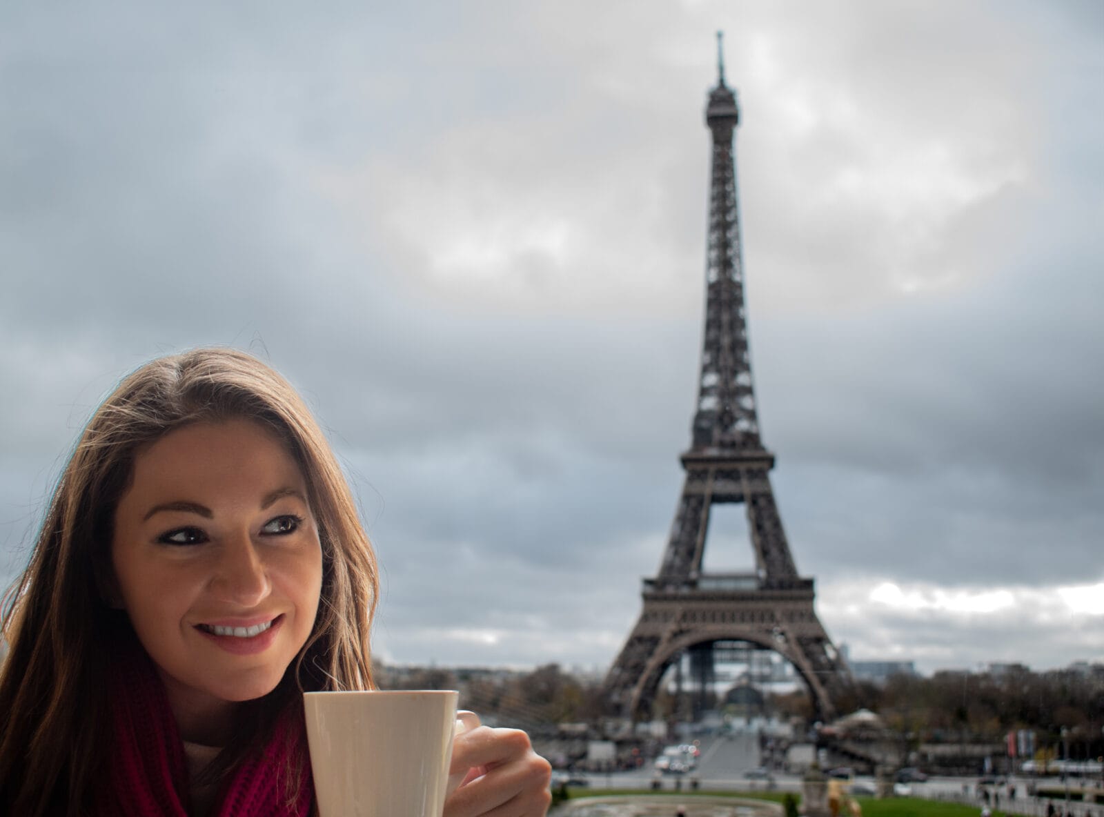 A woman holding a coffee cup with the Eiffel Tower behind her. 