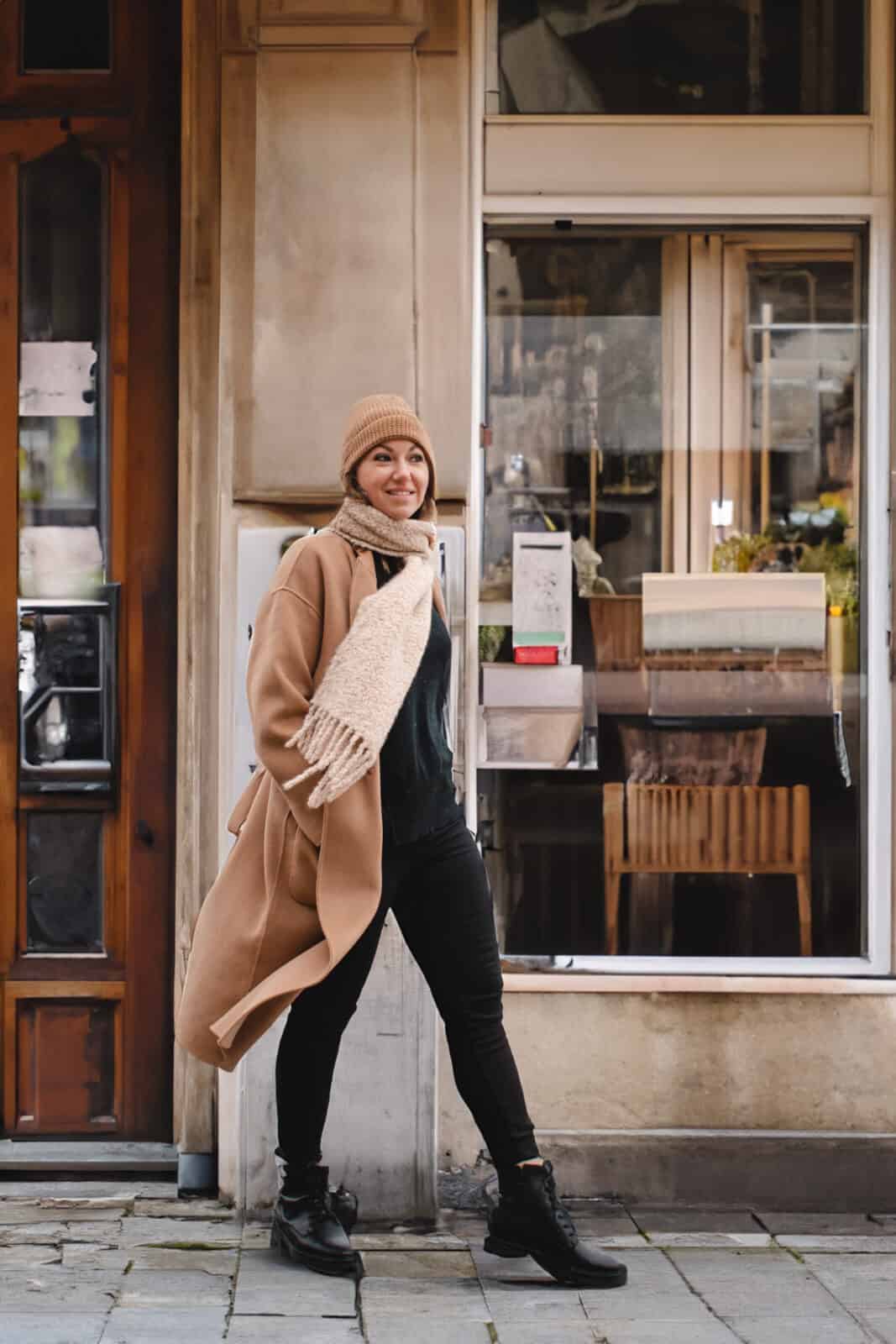 A woman walking in front of a cafe in Paris during the winter months. 