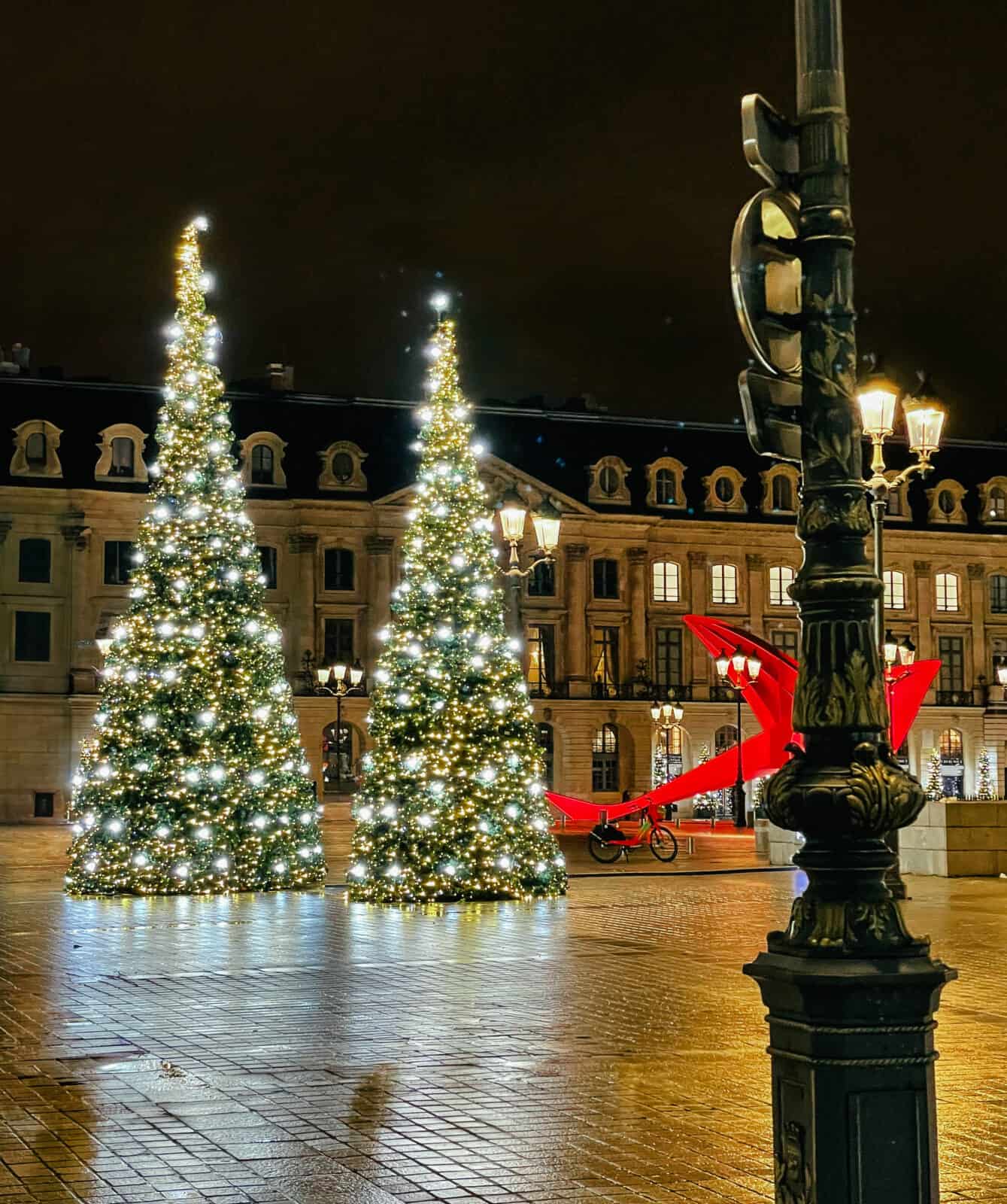 A plaza in Paris at night during the holiday season, with two Christmas trees lit up with lights. 